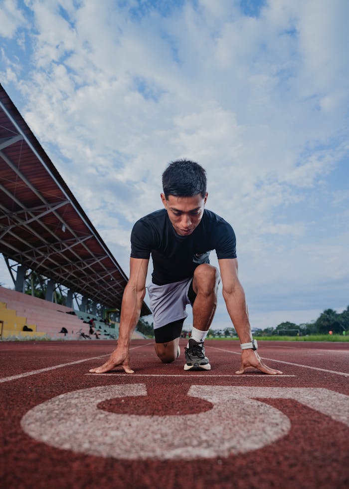 Focused male runner in starting position on outdoor track. Captures the essence of athletic dedication.